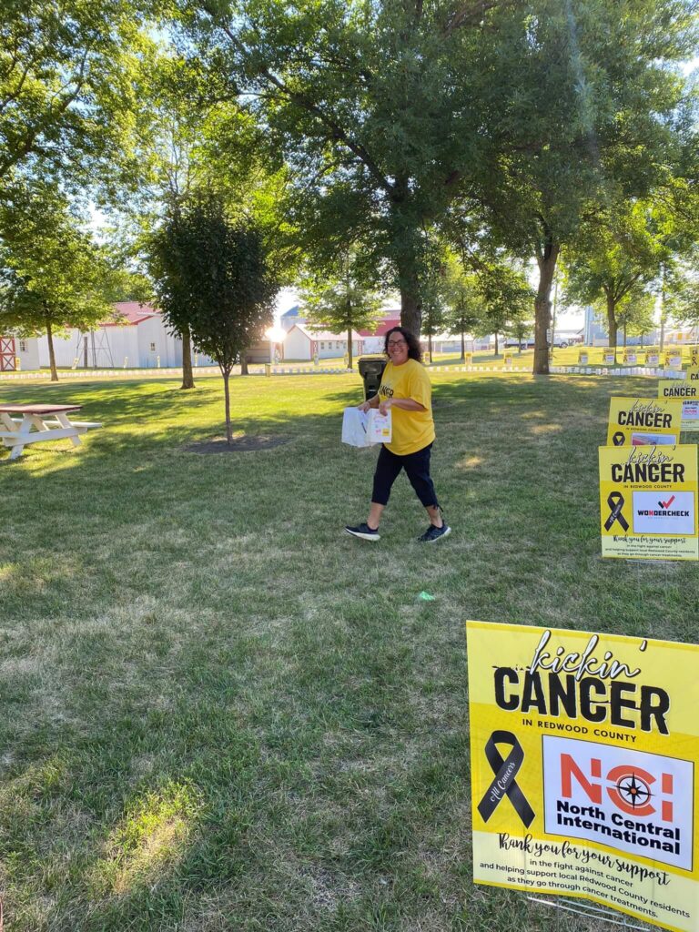 A woman walks through a park with signs promoting Kickin' Cancer