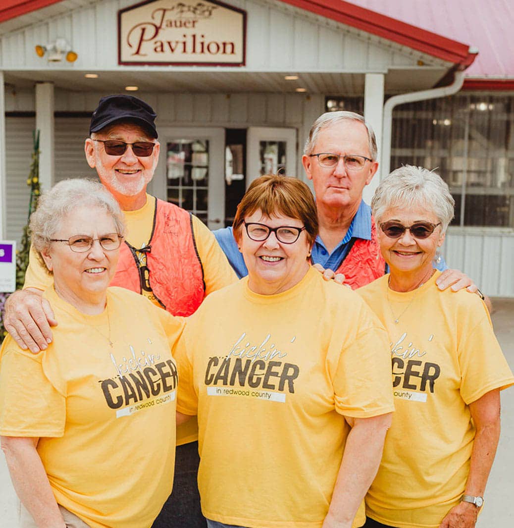 A group of people in yellow t-shirts posing in front of a cancer pavilion, expressing the essence of "about us.