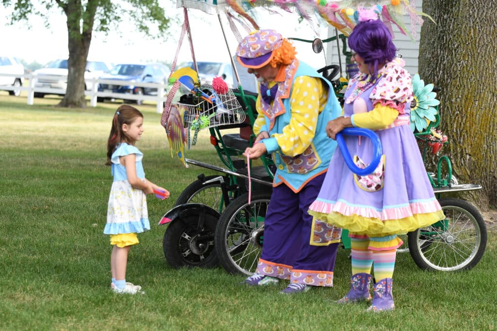 A little girl standing next to a clown at an event.